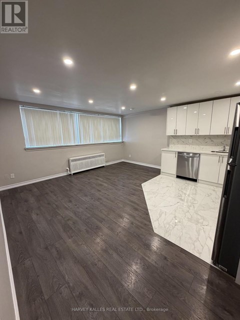 A spacious kitchen with white cabinets and a dark wood floor.