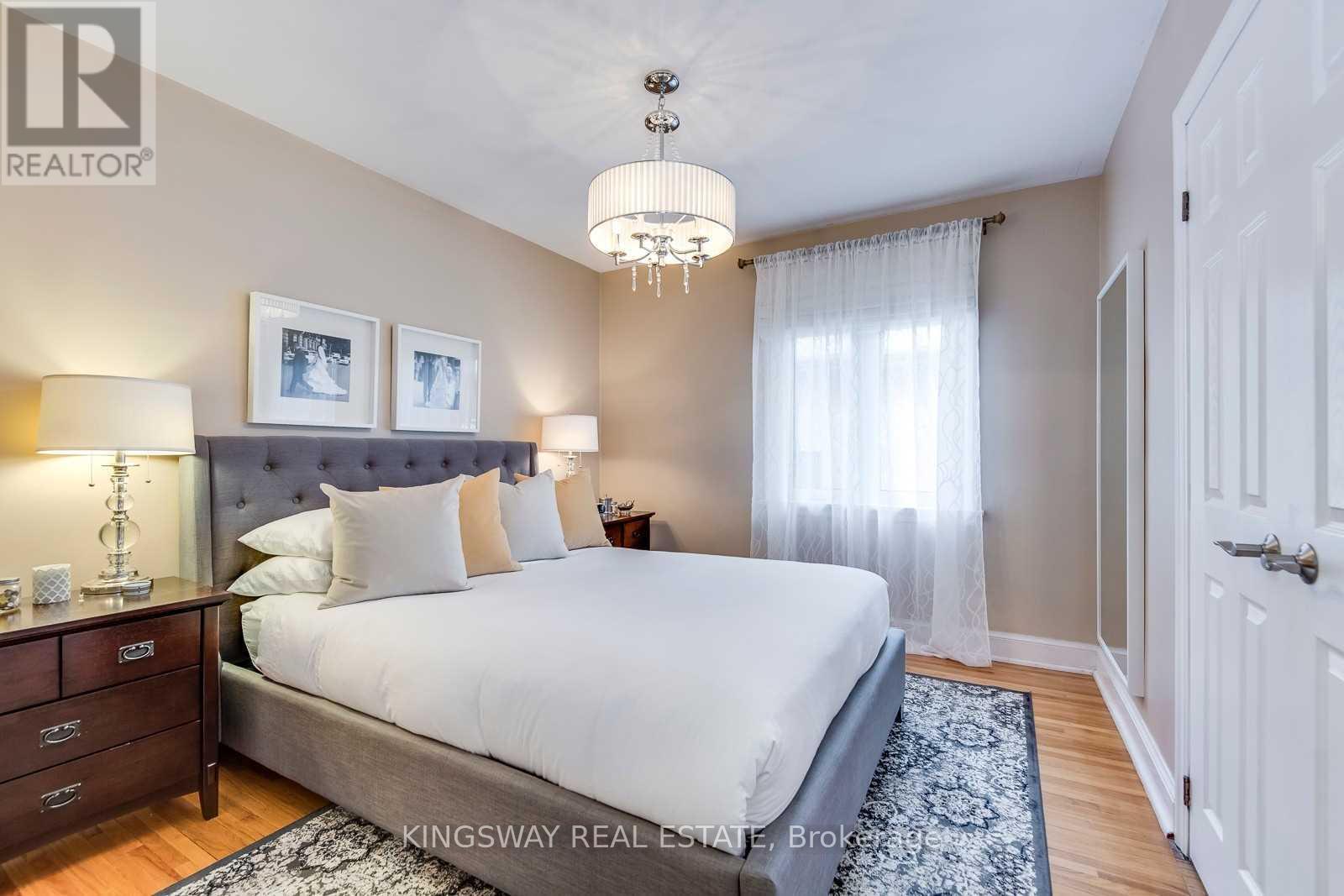 A bedroom with a large bed, a chandelier, and a nightstand with a lamp.