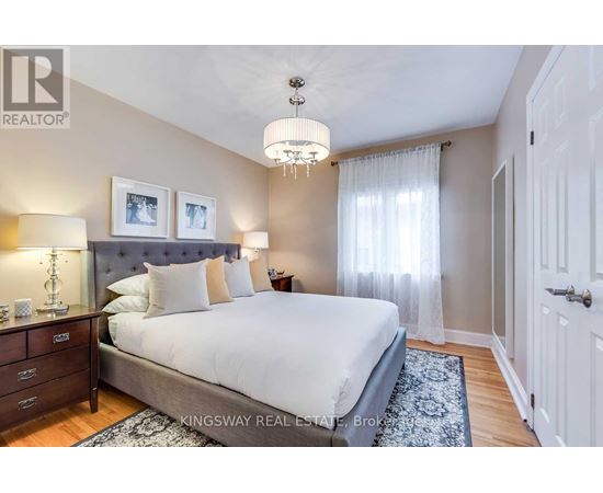 A bedroom with a large bed, a chandelier, and a nightstand with a lamp.