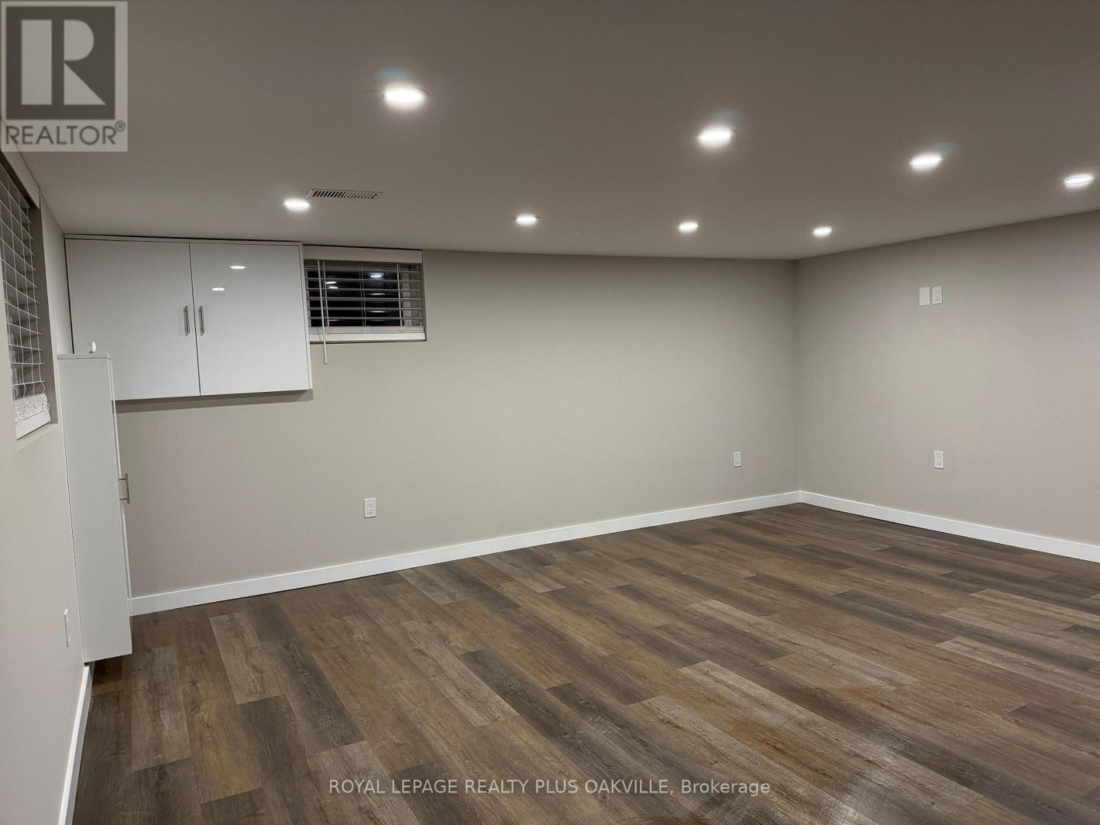 A room with wooden flooring and white walls, with a window and a cabinet.