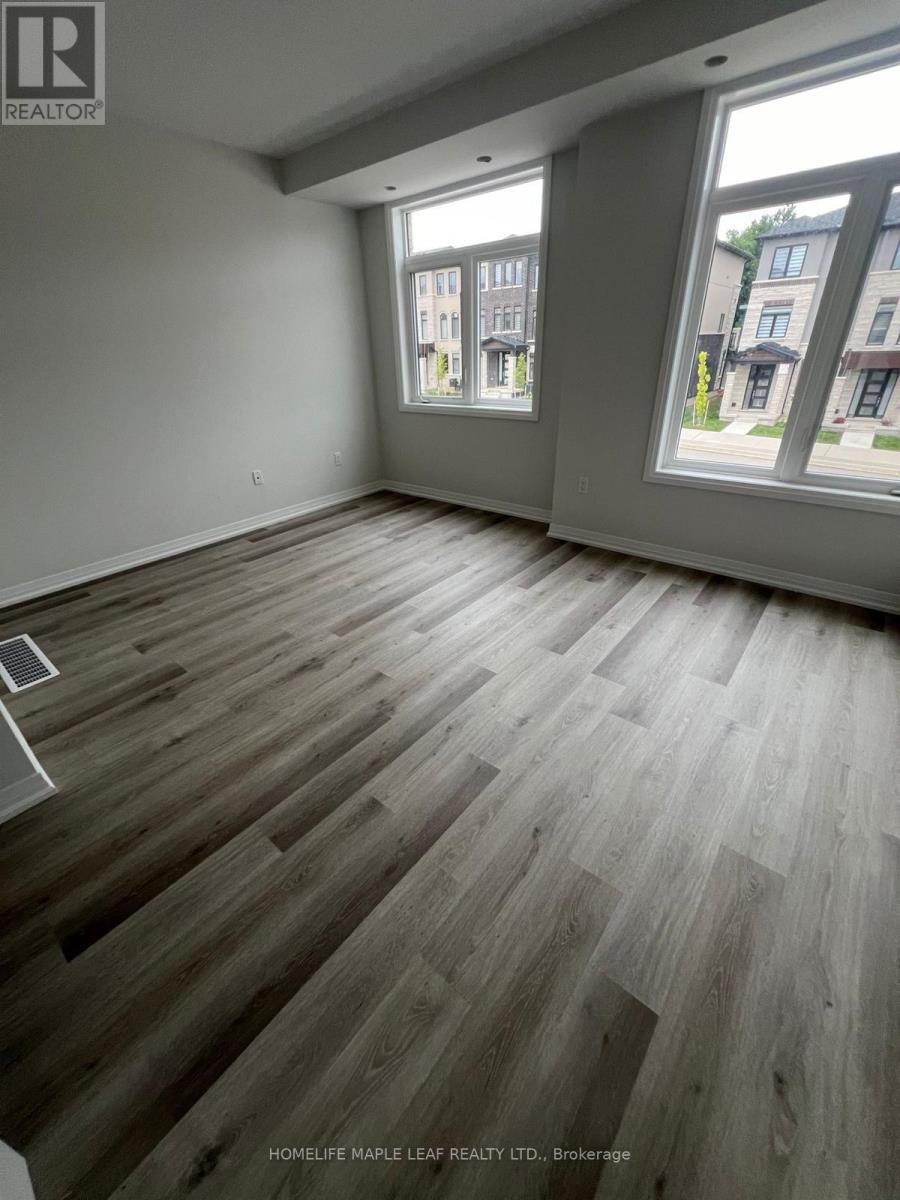 A room with wooden flooring and two windows showing a view of buildings outside.