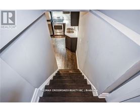 A staircase with a wooden handrail leads to a kitchen area.
