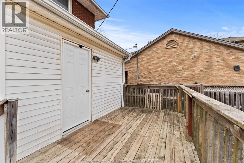 A wooden deck with a white door and a brick building in the background.