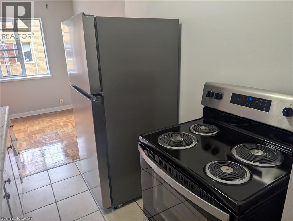 A black stove top oven with four burners and a silver refrigerator in a kitchen.