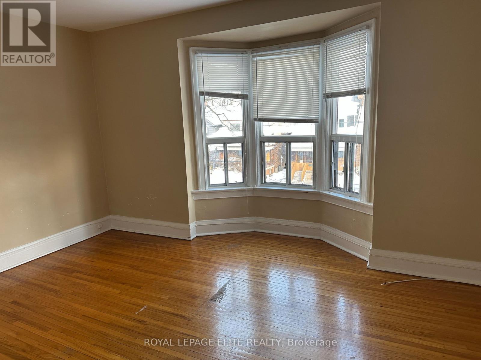 A room with wooden floors and a large window with blinds.
