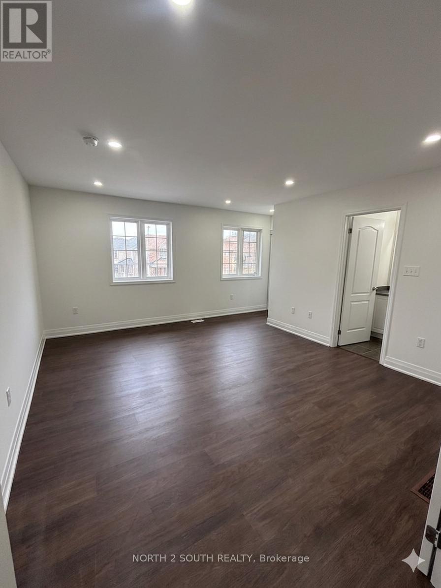 A spacious room with wood flooring and two windows.