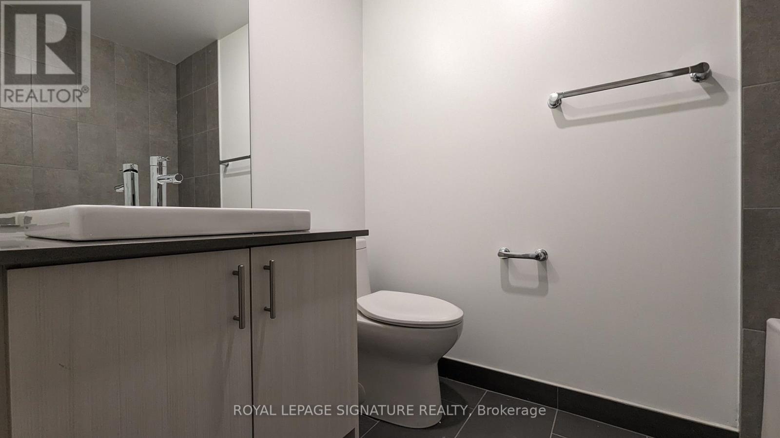 A white toilet sits in a bathroom with a sink and a towel bar.