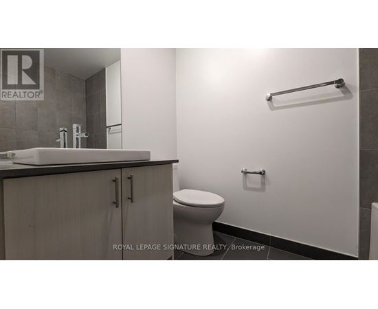 A white toilet sits in a bathroom with a sink and a towel bar.