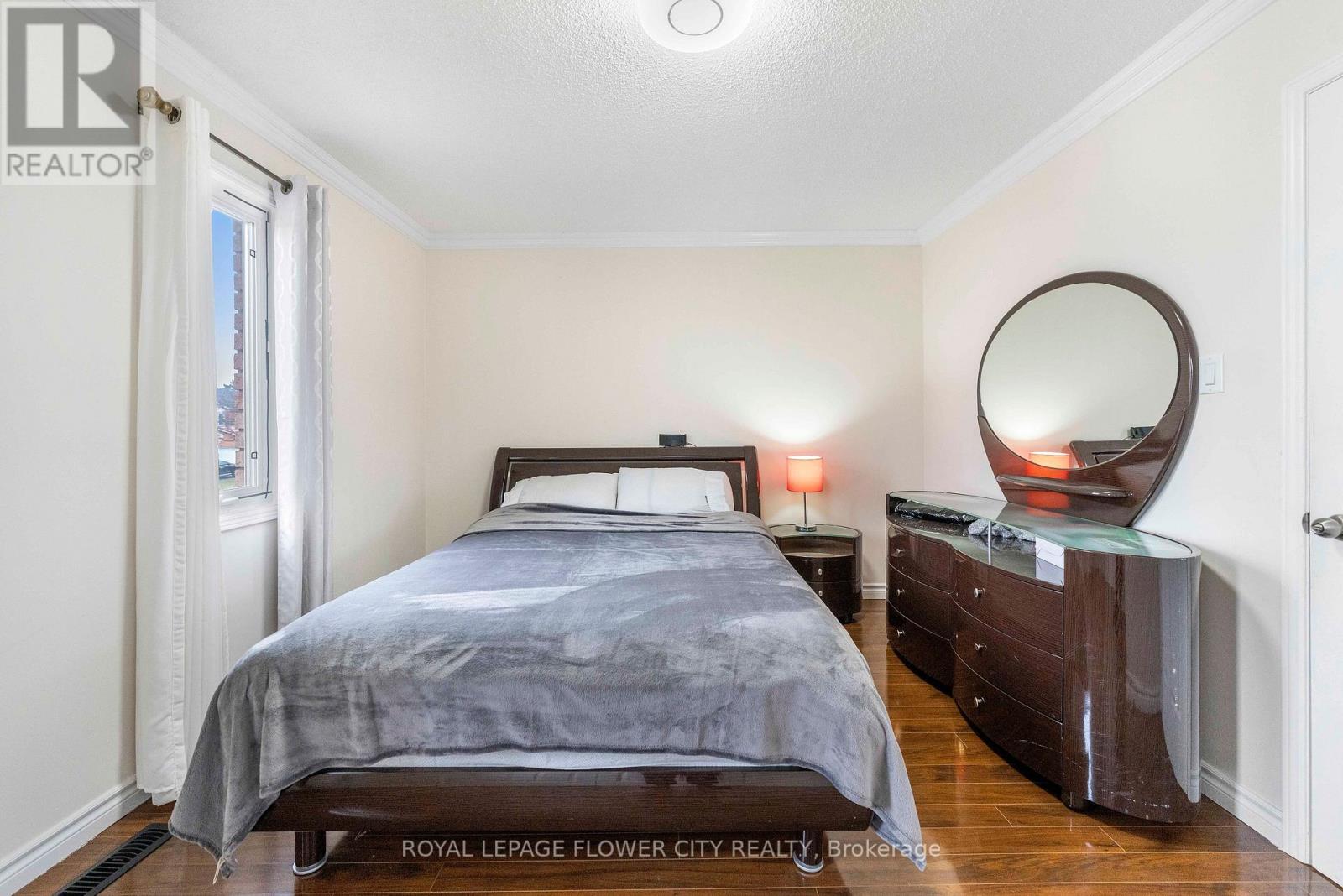 A bedroom with a bed, nightstand, and a round mirror on the dresser.