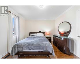A bedroom with a bed, nightstand, and a round mirror on the dresser.