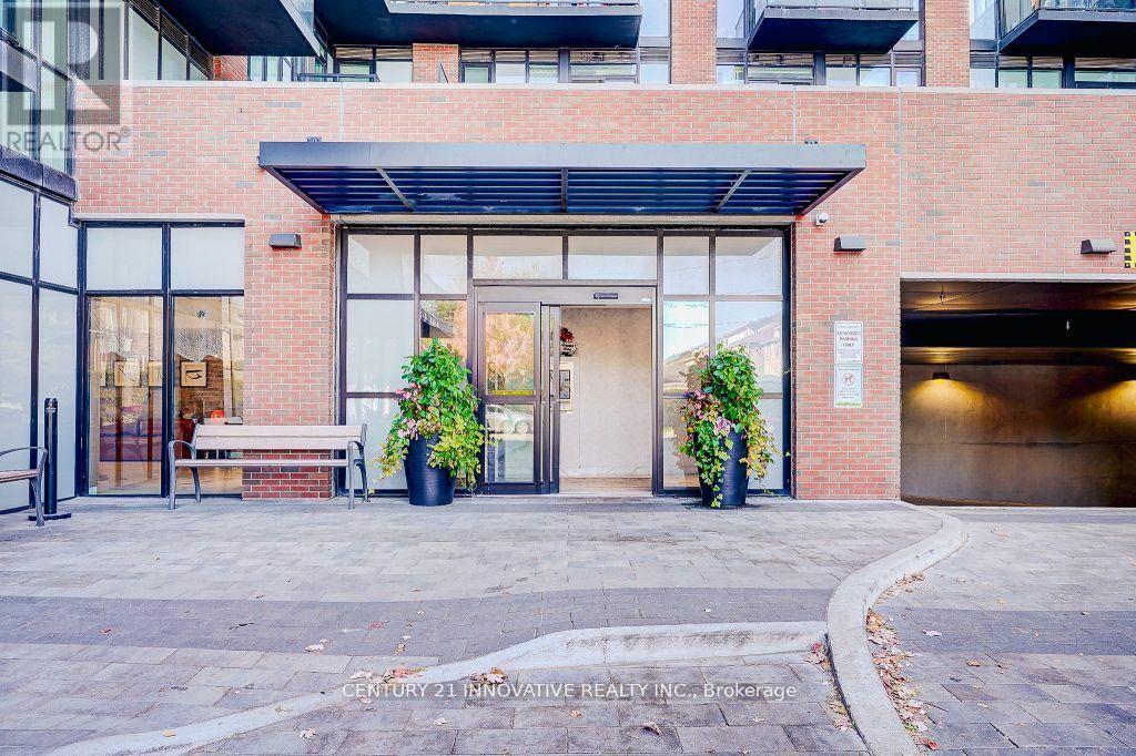 A brick building with a glass entrance and two potted plants on either side.
