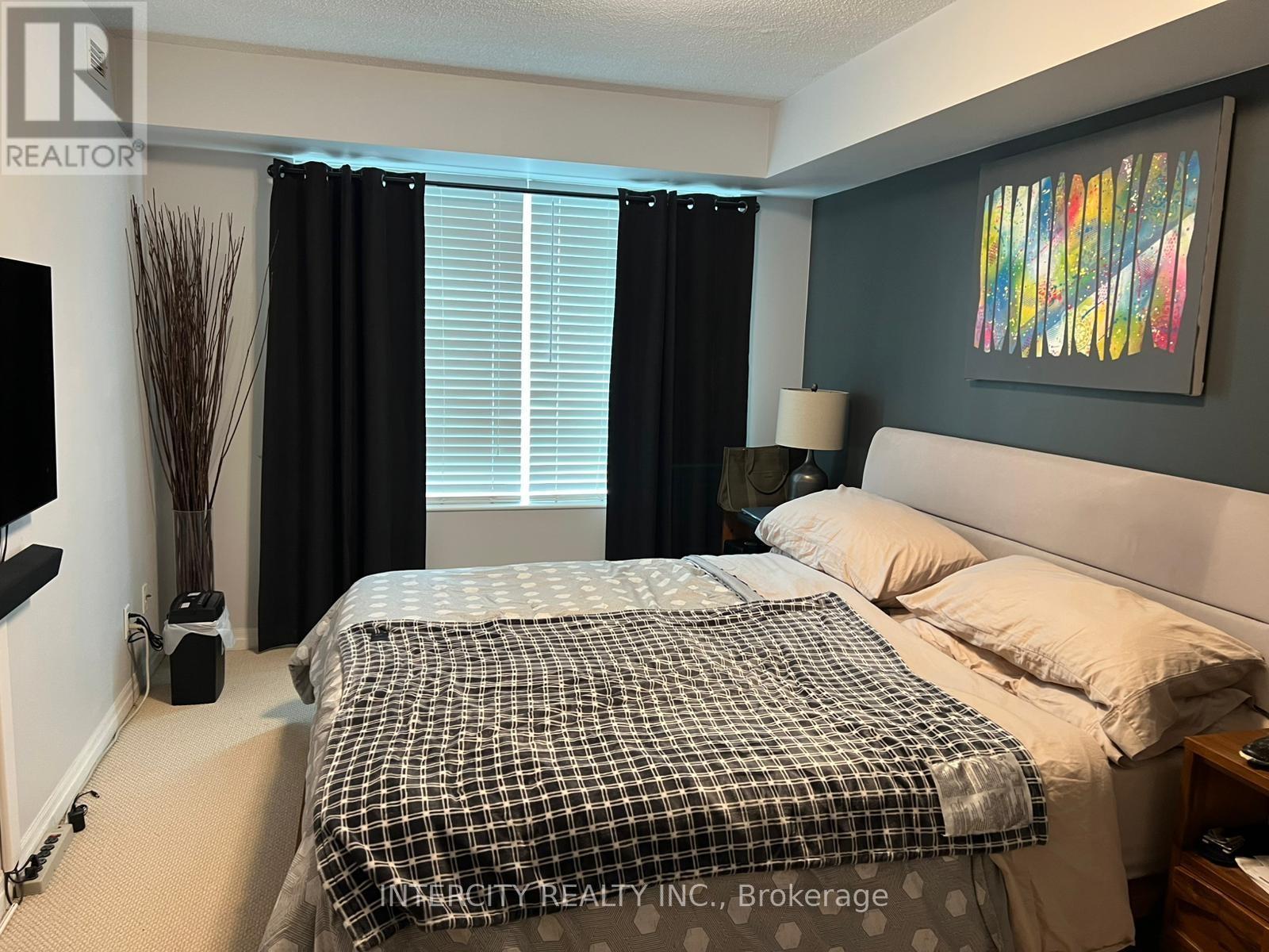 A bedroom with a bed, nightstand, and a painting on the wall.