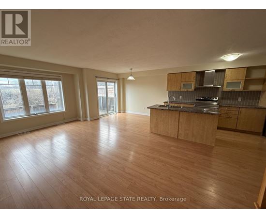 A spacious room with wooden flooring and a kitchen area with cabinets and a stove.
