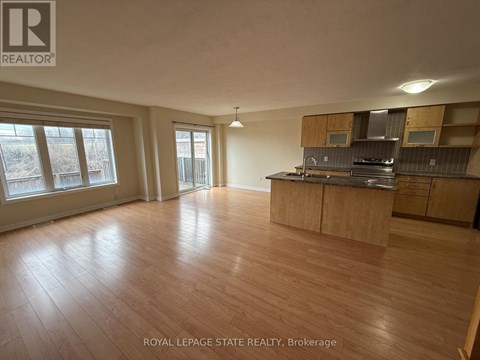 A spacious room with wooden flooring and a kitchen area with cabinets and a stove.