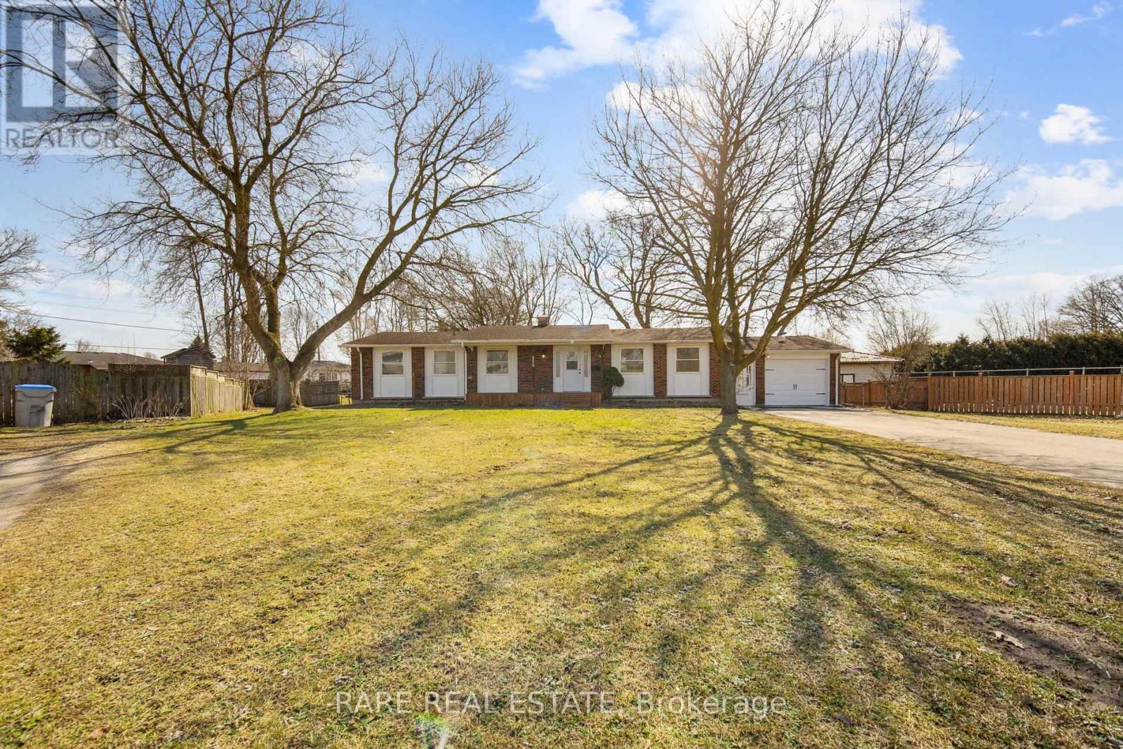 A house with a fence and trees in the background is for sale.