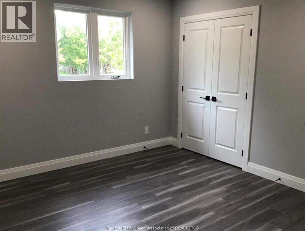 A room with a white door and a window with a view of trees outside.