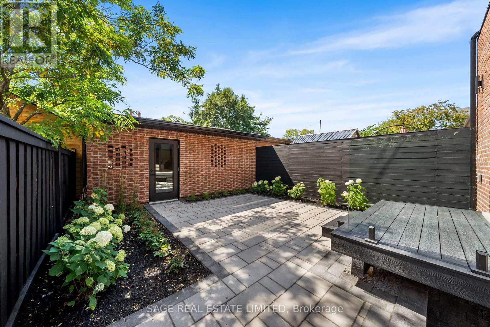 A backyard with a brick building, a wooden bench, and a black fence.