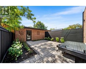 A backyard with a brick building, a wooden bench, and a black fence.