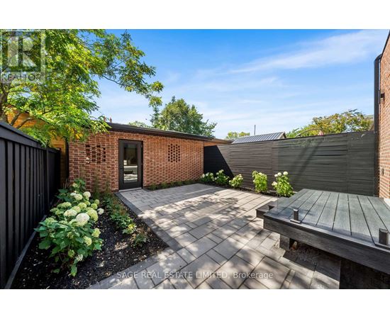 A backyard with a brick building, a wooden bench, and a black fence.