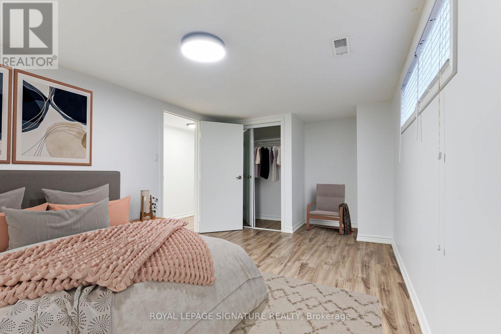 A bedroom with a bed covered in a pink blanket and a painting of sunglasses on the wall.