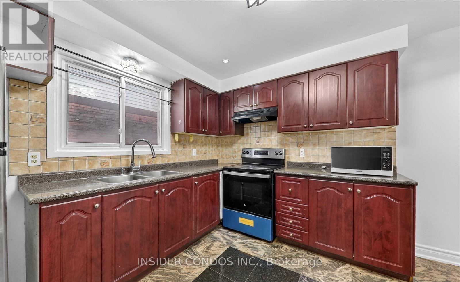 A kitchen with red cabinets and a black microwave.