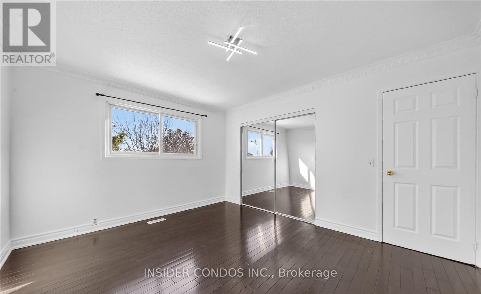 A spacious room with wooden floors and white walls, with a large window and a door visible.