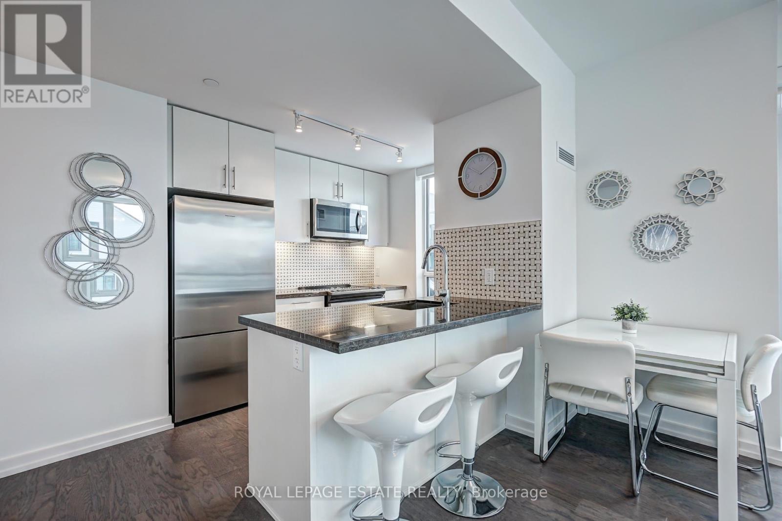 A modern kitchen with white chairs and a black countertop.