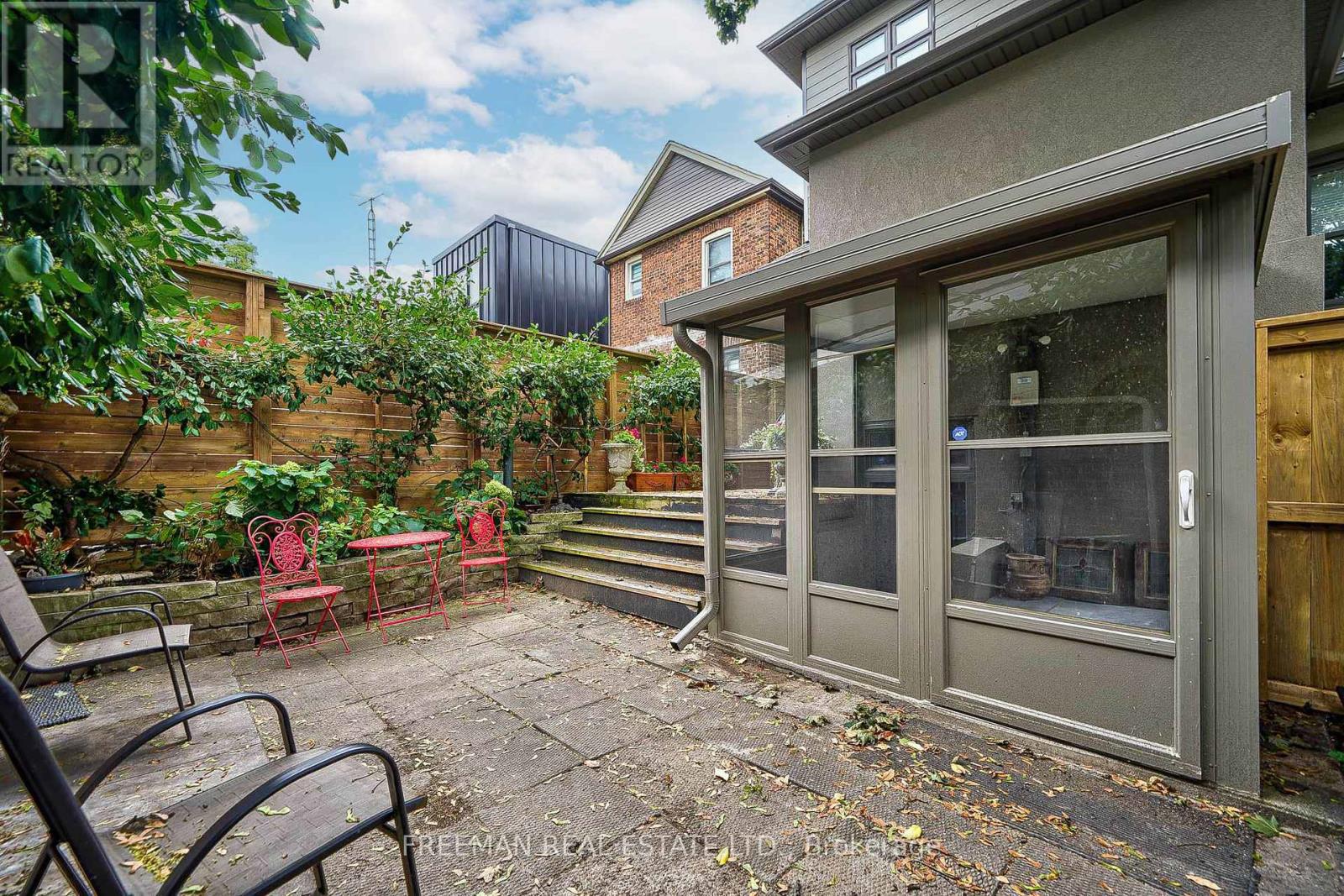 A patio with a table and chairs is surrounded by a wooden fence and a brick building.