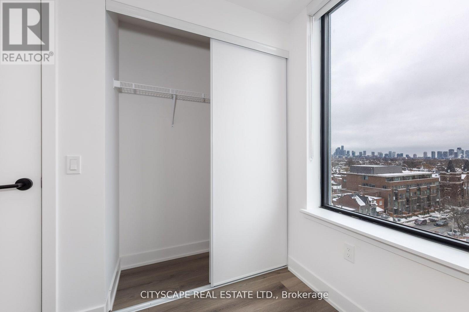 A white bedroom with a window overlooking a cityscape.