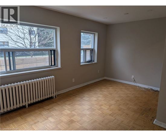 A room with wooden flooring and two windows.