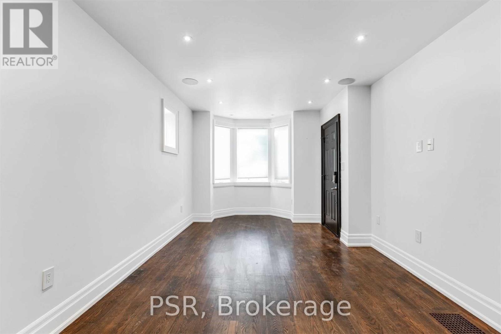 A room with wooden floors and white walls, with a door on the right side.