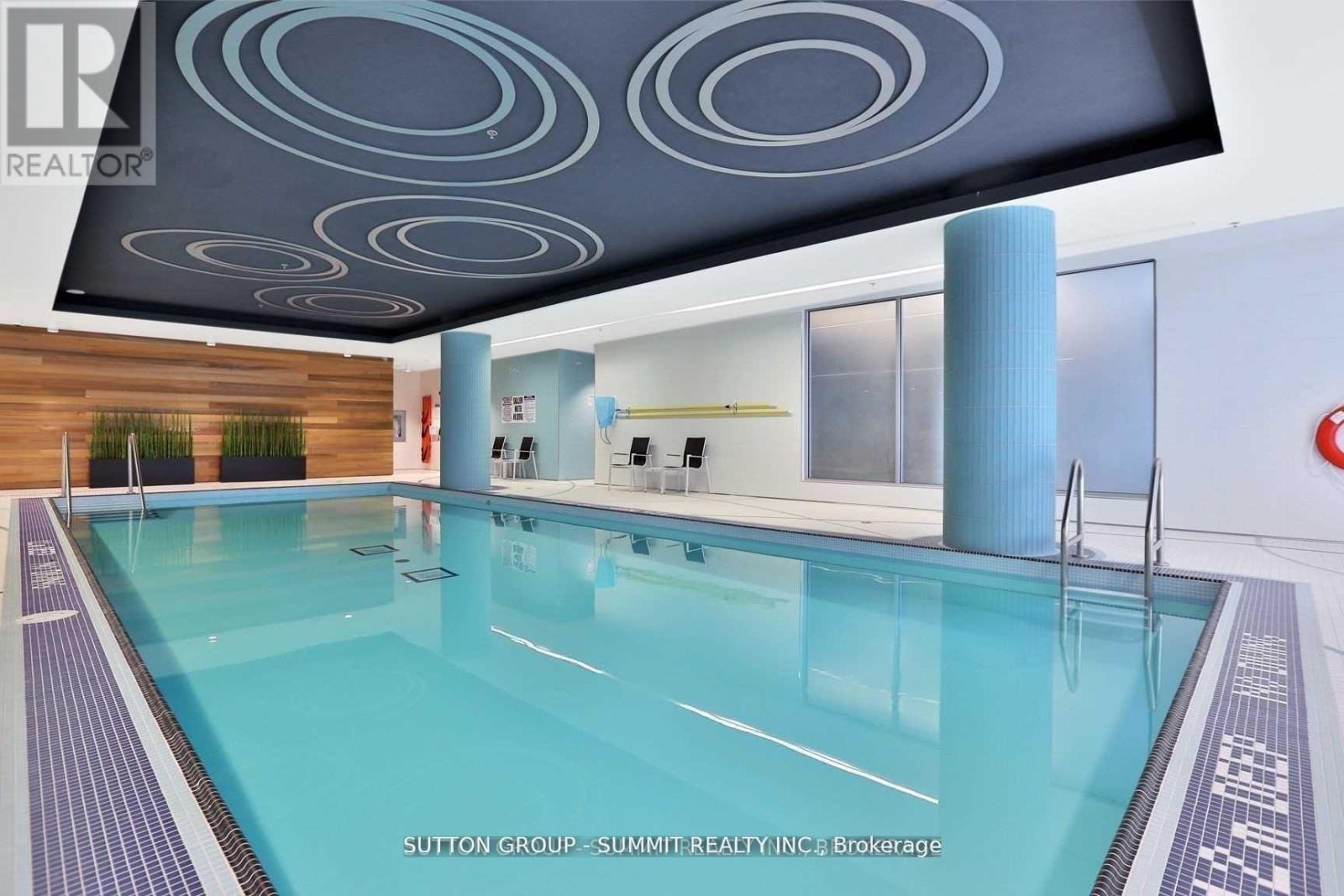 A swimming pool in a room with a ceiling design and a brokerage sign.