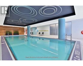 A swimming pool in a room with a ceiling design and a brokerage sign.