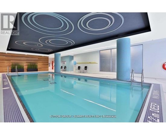 A swimming pool in a room with a ceiling design and a brokerage sign.