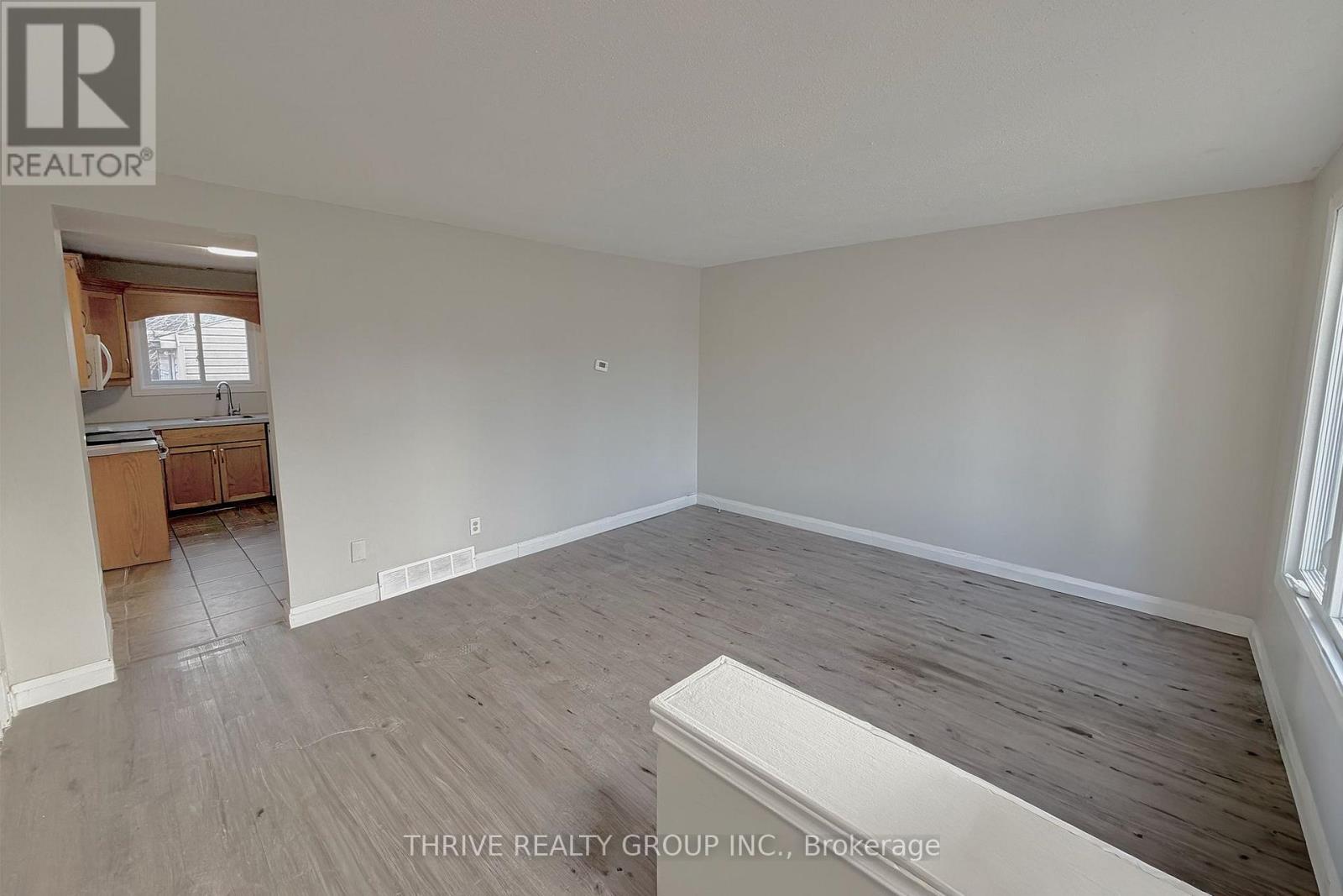 A room with a wooden floor and white walls, with a window on the left side.