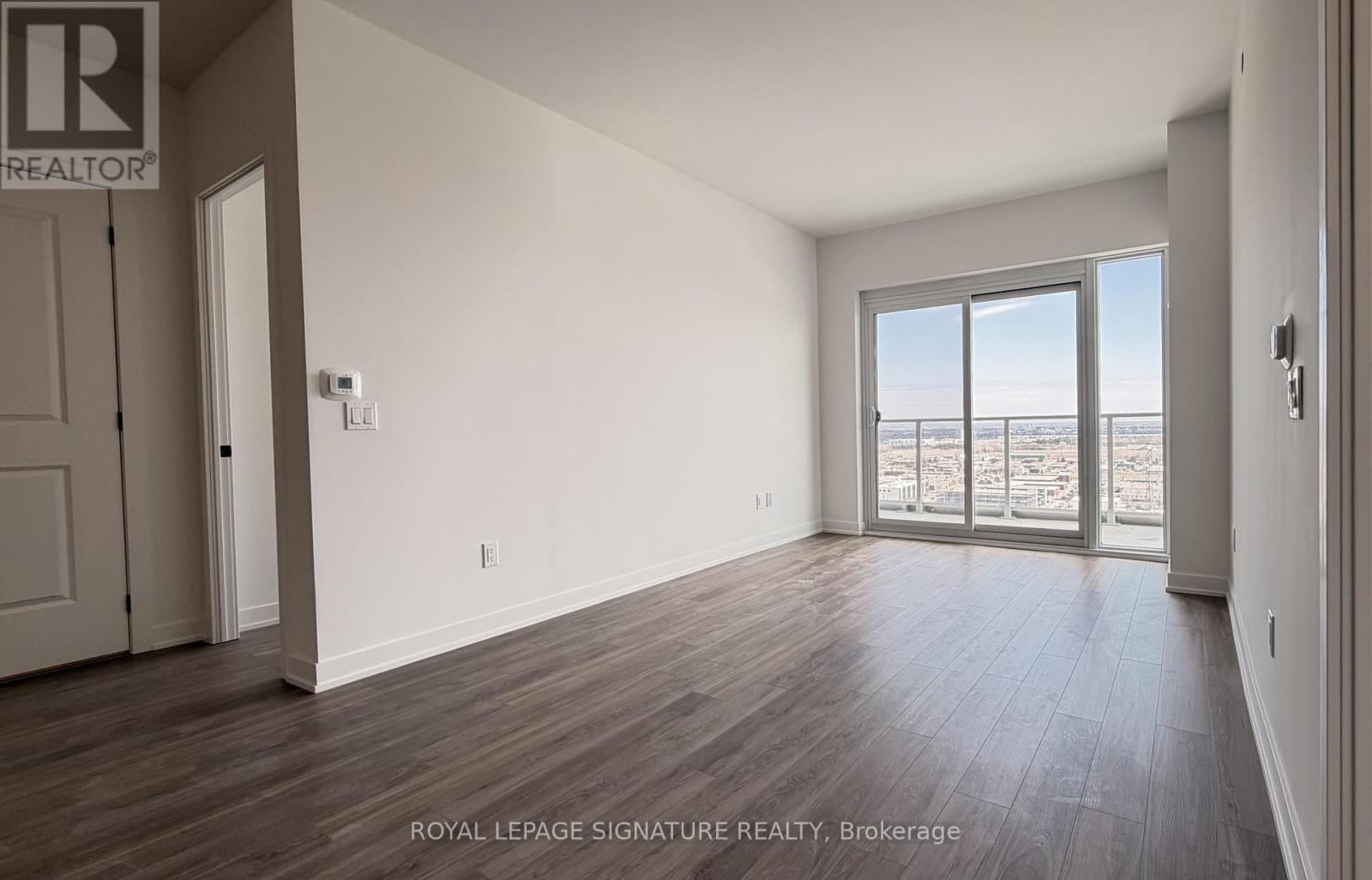 A spacious room with wooden flooring and a sliding glass door leading to a balcony.