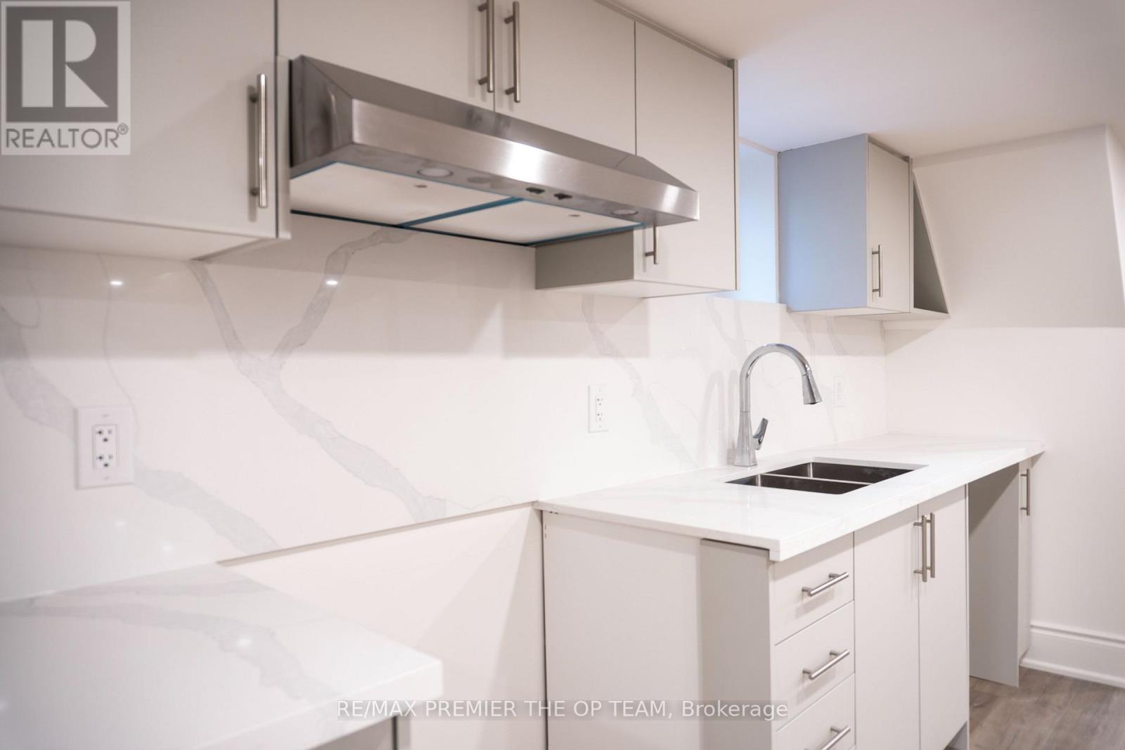 A white kitchen with a sink and a stainless steel range hood.