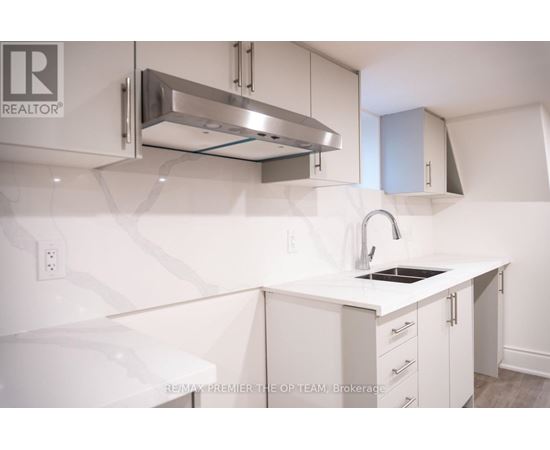 A white kitchen with a sink and a stainless steel range hood.