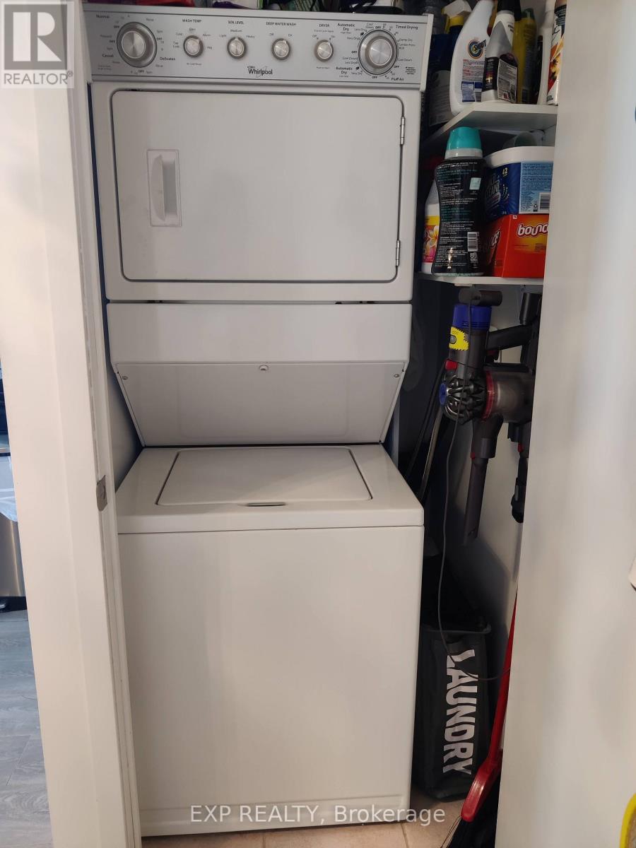 A white dryer is in a small space with a vacuum cleaner to the right.