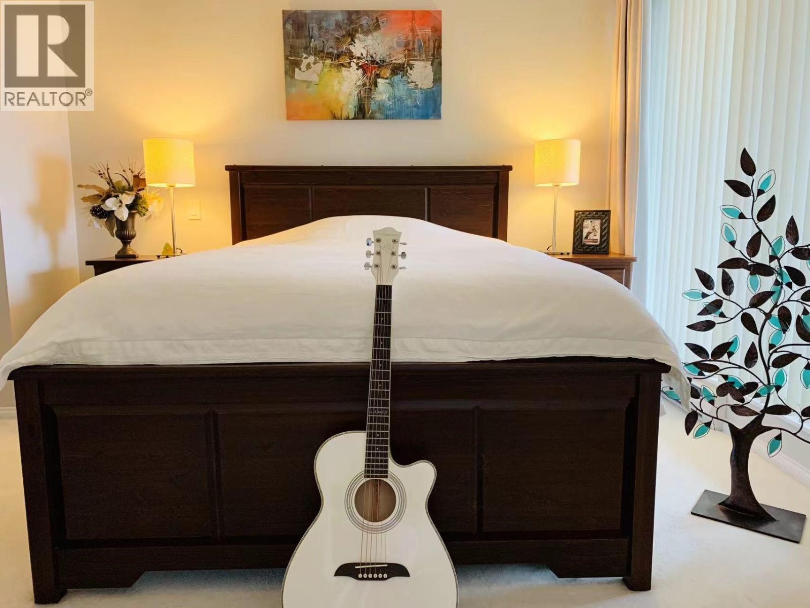 A white guitar is placed on a bed in a bedroom.