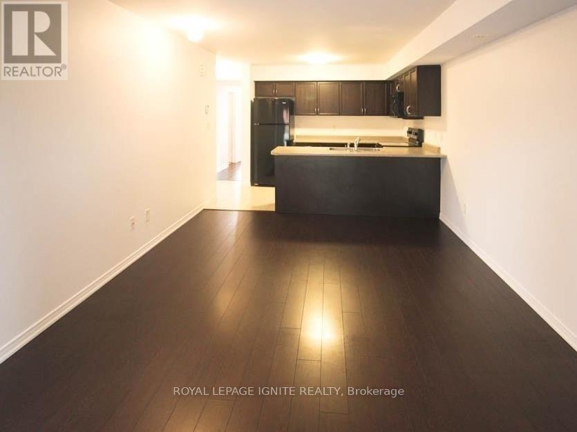 A spacious room with wooden flooring and a kitchen area in the background.
