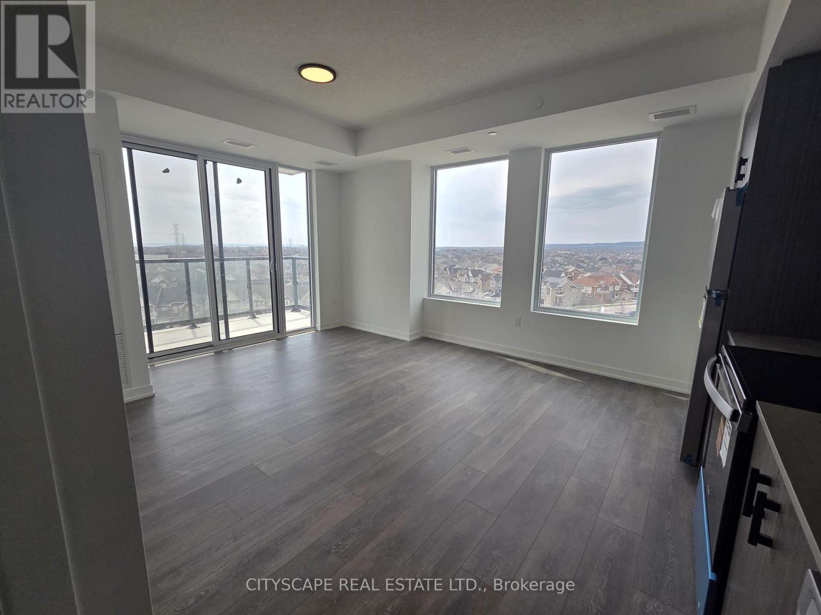 A spacious room with wooden flooring and large windows overlooking a cityscape.
