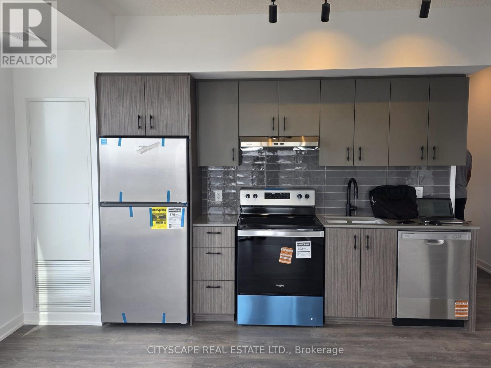 A kitchen with a stainless steel refrigerator, black stove, and grey cabinets.