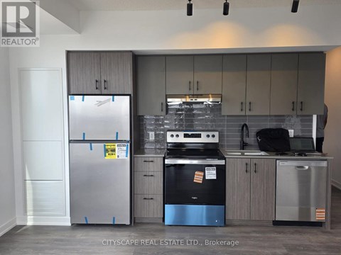A kitchen with a stainless steel refrigerator, black stove, and grey cabinets.