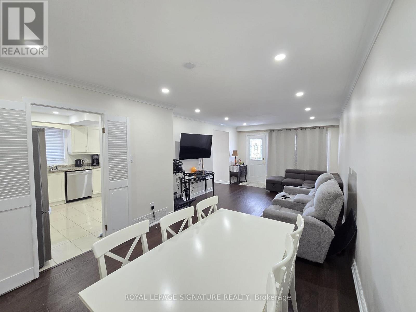 A white dining table is surrounded by grey chairs in a spacious room.
