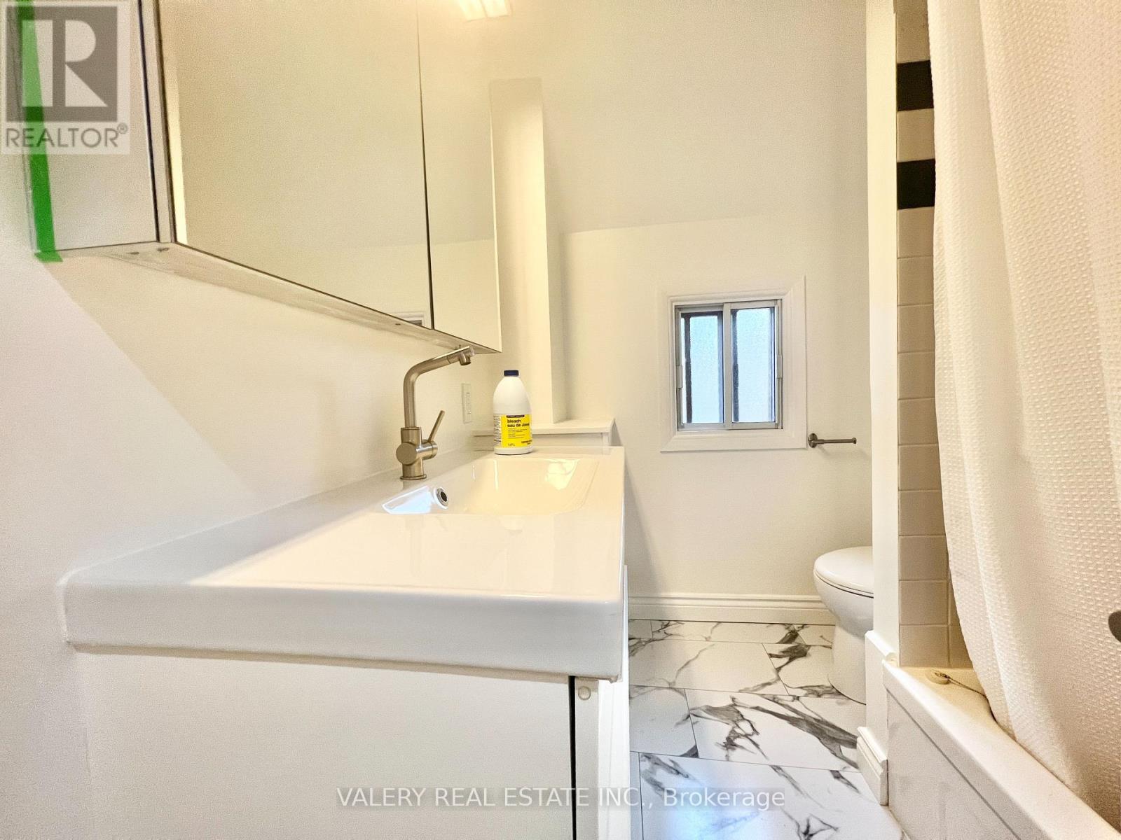 A white bathroom with a marble floor and a small window.