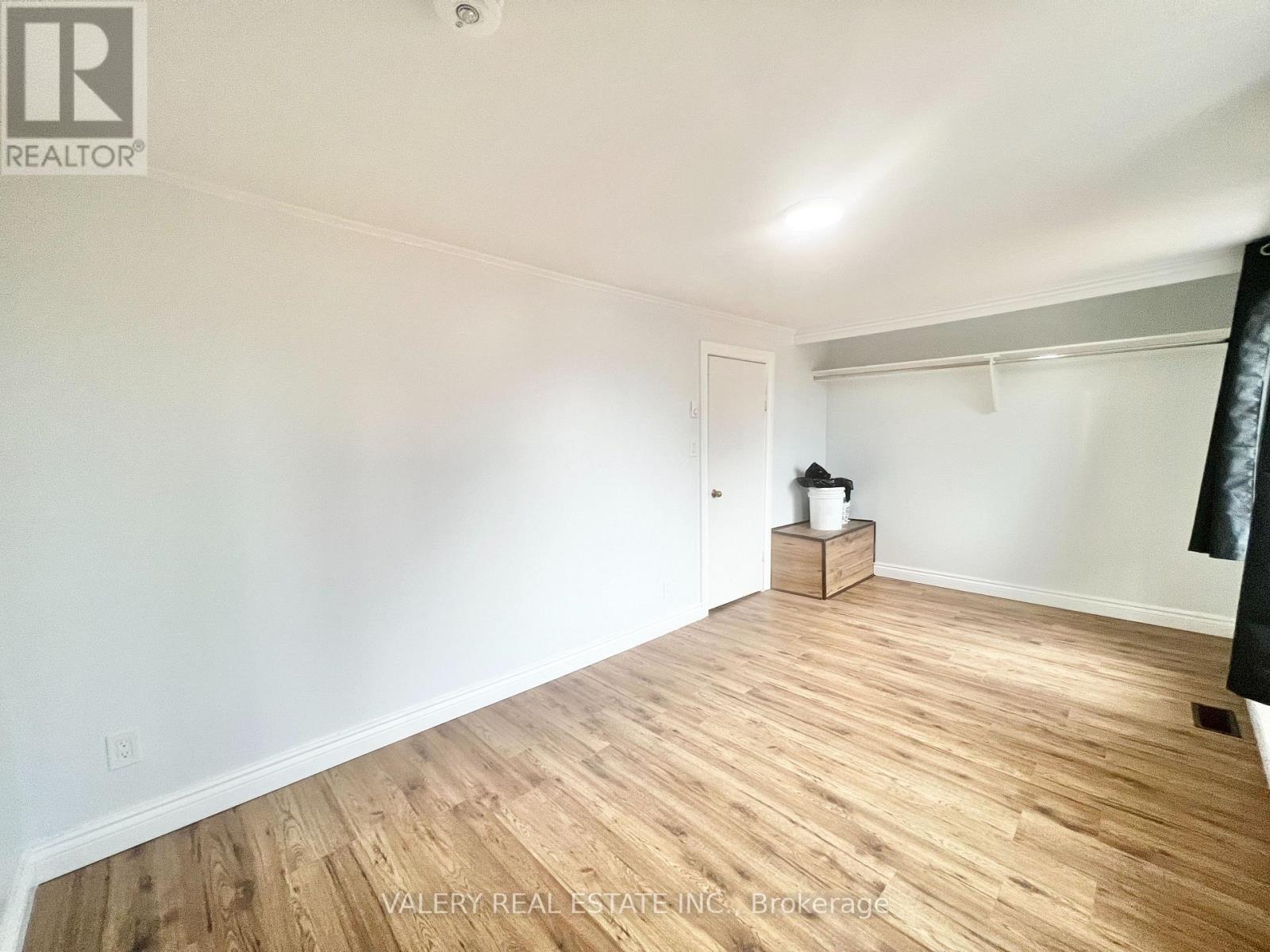 A room with wooden flooring and white walls, with a small wooden cabinet and a white bucket on a small table.