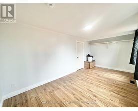 A room with wooden flooring and white walls, with a small wooden cabinet and a white bucket on a small table.