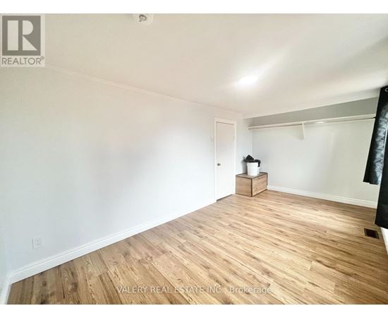 A room with wooden flooring and white walls, with a small wooden cabinet and a white bucket on a small table.