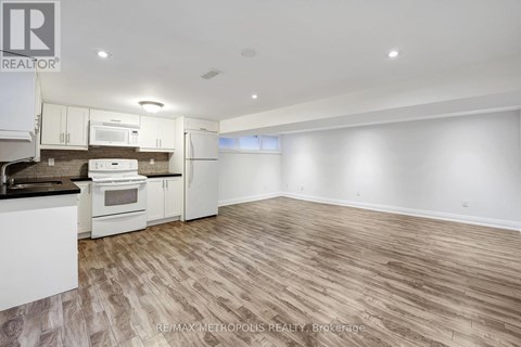A spacious kitchen with white appliances and wooden flooring.